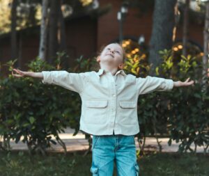 Girl standing outside with arms out. She is looking up at the sky.