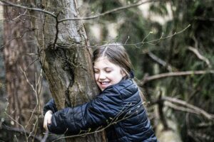 A girl hugging a tree. Leaves are budding on the tree.
